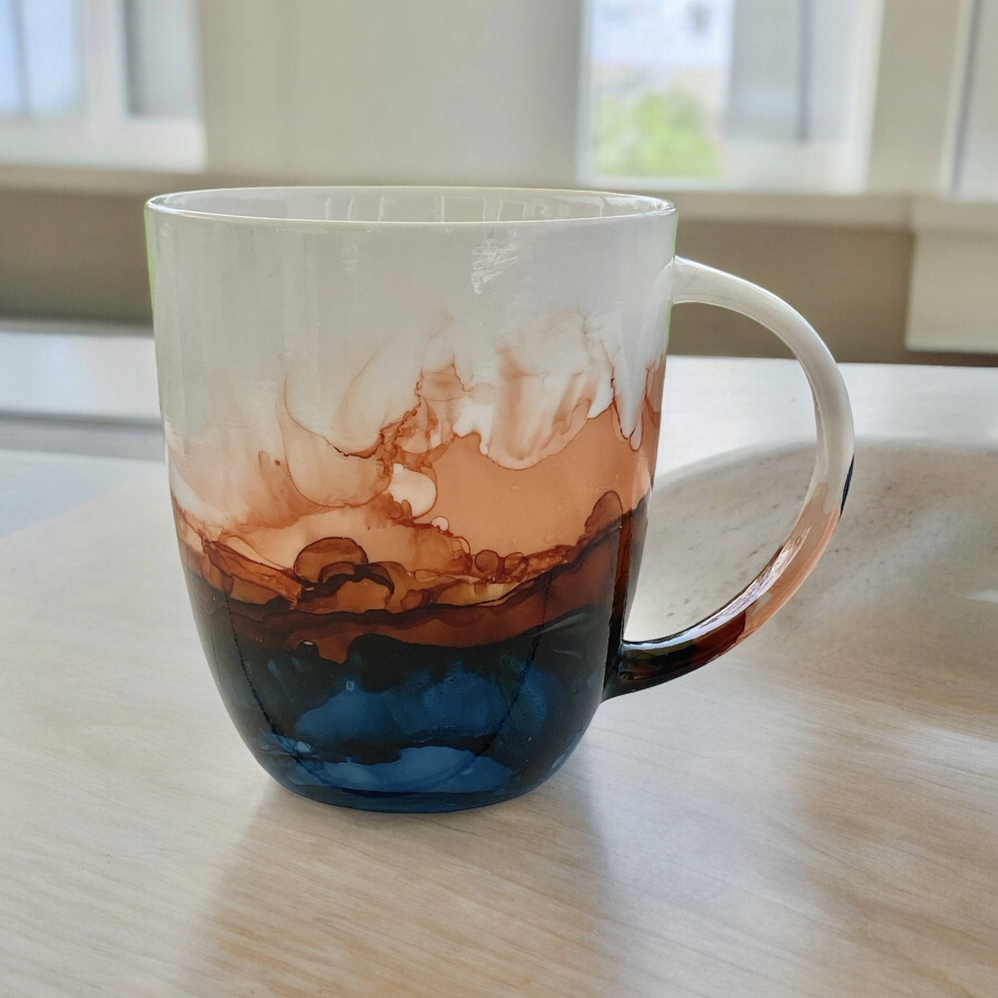 Ceramic Coffee Mug on a wood counter top. Mug has been painted in blues and oranges.